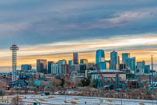 Early Morning Sunrise Shot of Downtown Denver Skyline with Vibrant-Colored Amusement Park Rides in the Foreground on a Snowy Winter Day