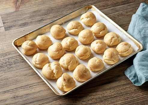 freshly baked cream puffs on baking pan on wooden kitchen table