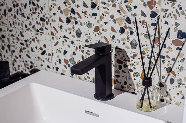 черный смеситель на умывальнике в ванной комнате, стена украшена плиткой в стиле терраццо - bathroom black faucet стоковые фото и изображения