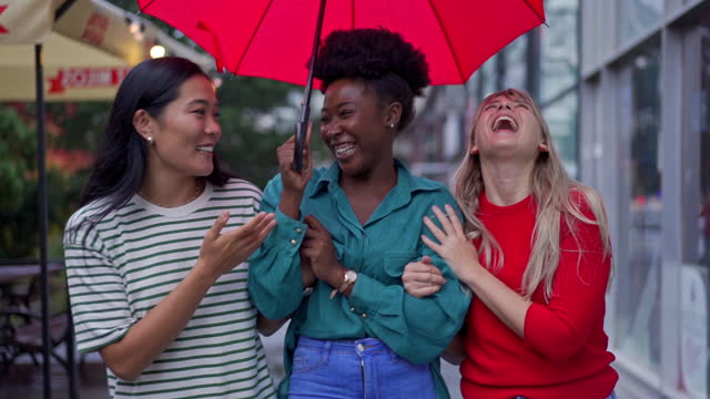 Portrait of an modern and urban city multiracial female friends walking under umbrella during rainy day in the city