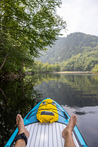 POV of man paddleboarding and kayaking on the River in Summer. Only the man’s legs and feet are visible. Rivière Vallée Bras-du-Nord, Quebec, Canada
