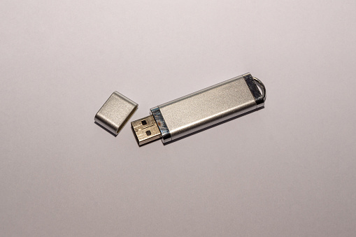 A silvery USB flash drive with an open cap, fairly used with a worn casing coating, lies on a white surface, selective focus