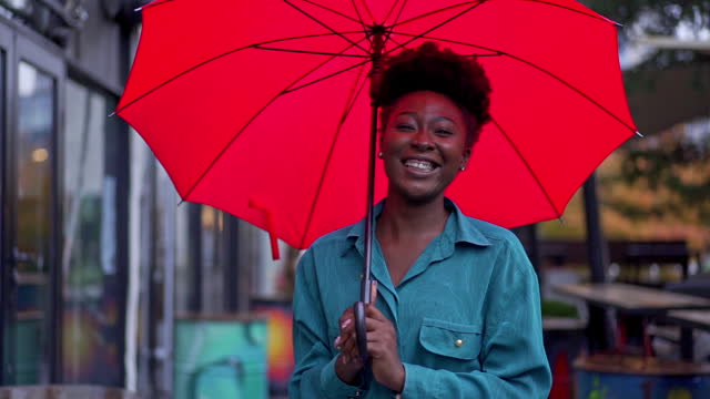Carefree and smiling young woman of Black ethnicity standing under umbrella