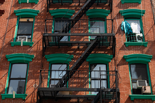 The exterior of an old brick apartment building with a fire escape on the Lower East Side of New York City with clothes hanging outside a window