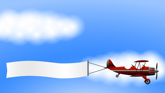 A red biplane plane with an advertising banner on the background of clouds