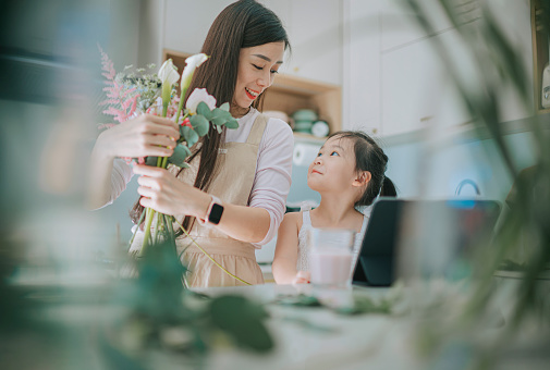 Asian female florist bonding with daughter while working flower arrangement in kitchen