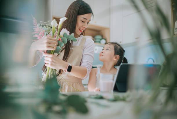 florista feminina asiática se conecta com filha enquanto trabalha arranjo de flores na cozinha - flower arrangement fotos - fotografias e filmes do acervo