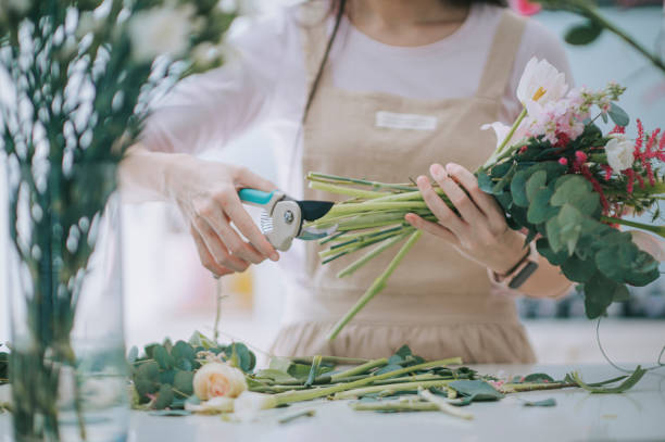 schließen sie asiatische chinesische floristin, kleinunternehmerin, die blumensträuße in der küche zu hause schneidet und arrangiert. tägliche routine der führung eines kleinen unternehmens von zu hause aus arbeiten - florist stock-fotos und bilder