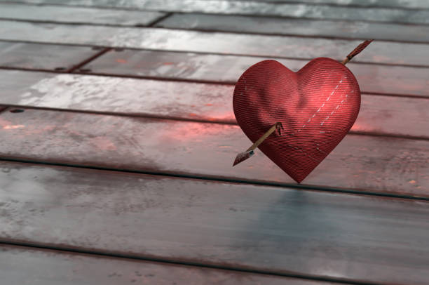 Red heart symbol broken into small splinters of glass from a shot from a pistol with a hole from a bullet isolated on a black background. Allegory of the unhappy love of a broken heart.