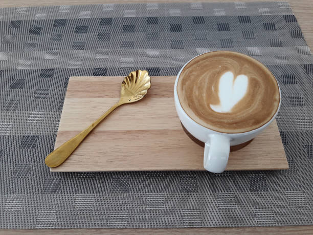 Latte coffee in a white heart shape ceramic cup on a wooden plate