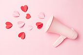 Valentine's Day background of megaphone and heart shaped confetti on pink background.