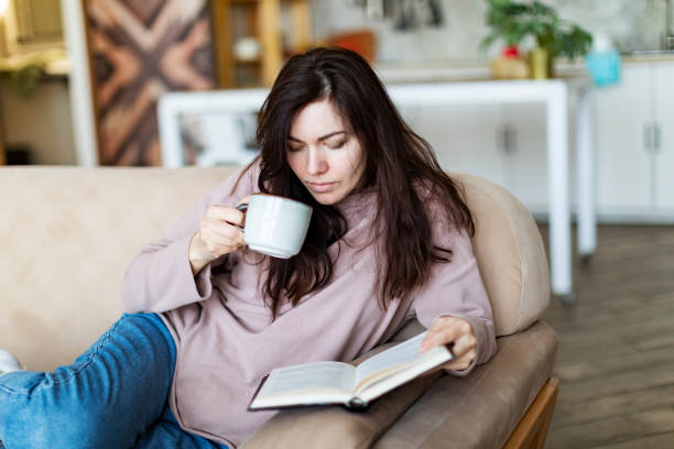 istock Young woman resting at home reading book 1364898782