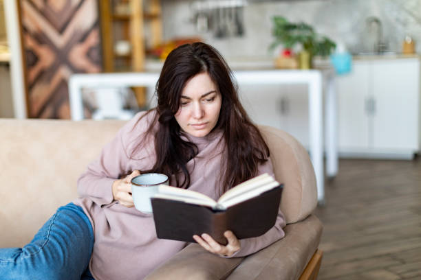 istock Young woman resting at home reading book 1364899299