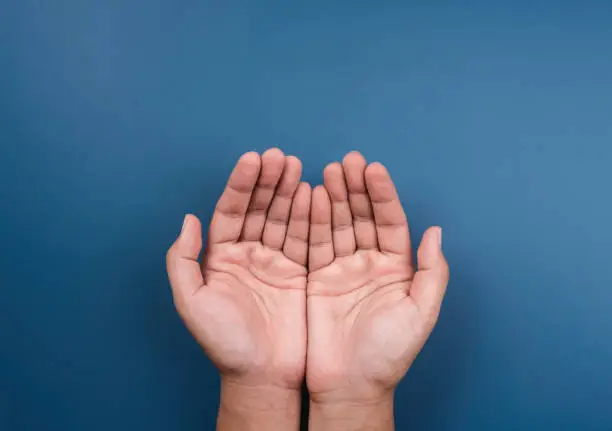 Photo of Two empty holding hands gesture isolated on blue background, top view. Giving, requesting, praying, making a wish hand, begging, care concept, outstretched cupped hands.