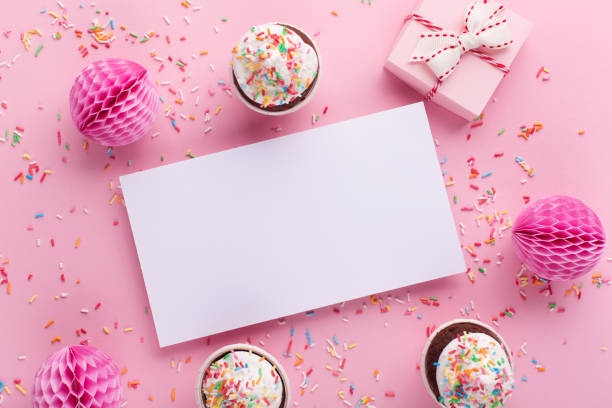 istock Empty white blank, gift box, paper decorations and cupcakes on pink sprinkles background. 1364904074