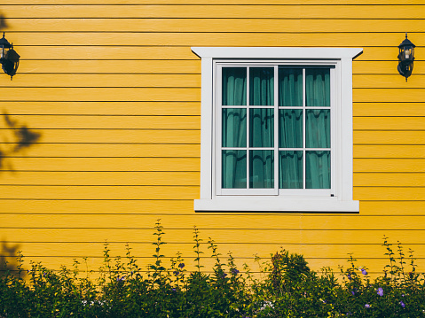 A white house window with glass, green curtain decoration with wall lamps on the yellow wooden resident, view from outdoor.