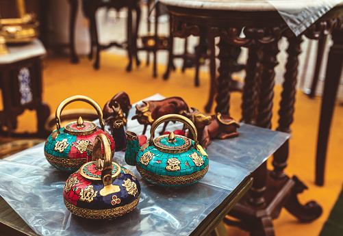 Beautiful hand crafted designer tea pots on display at home decor shop. Traditional Indian handmade kettles with colourful stones and intricate patterns at a festival fair.