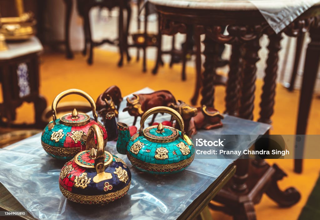 traditional indian colourful tea pots on display at a store. Beautiful hand crafted designer tea pots on display at home decor shop. Traditional Indian handmade kettles with colourful stones and intricate patterns at a festival fair. Home Decor Stock Photo