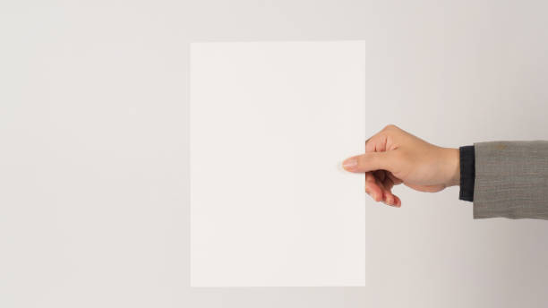 istock Space for text. The hand is wearing a gray suit and holding blank board A4 paper on white background. 1364906351