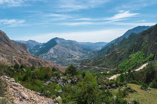 Amazing view from pass to mountain valley in sunlight and great mountain silhouettes on horizon. Lush greenery and mountain slopes. Big rocky mountains and epic deep gorge.