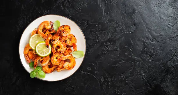 Grilled tiger shrimps with spice and lime. Black background. Top view, space for text.