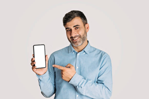mann hält und schaut auf smartphone mit mockup auf weißem hintergrund - isolated cheerful businessman smiling stock-fotos und bilder