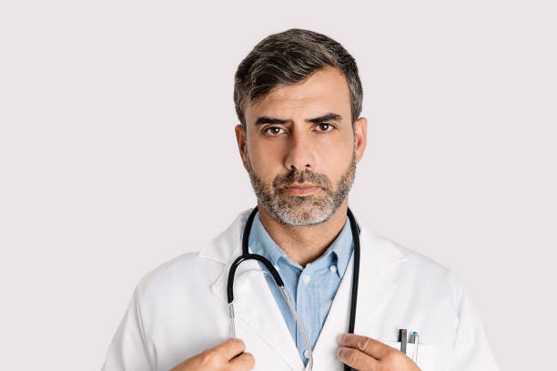 headshot eines ernsthaften männlichen arztes auf weißem hintergrund - doctor male doctor mature men portrait stock-fotos und bilder