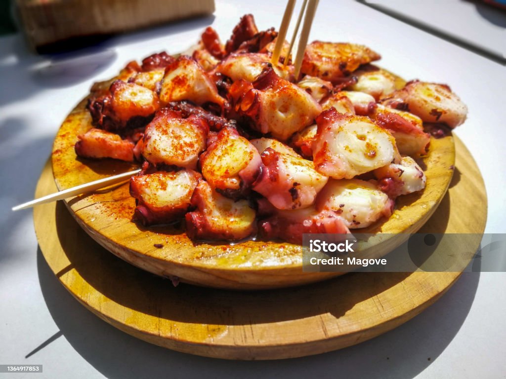 Polbo a feira (Galician style octopus) with paprika and oil Polbo a feira (Galician style octopus) with paprika and oil with chopsticks on wooden plate served outdoors. Appetizer Stock Photo