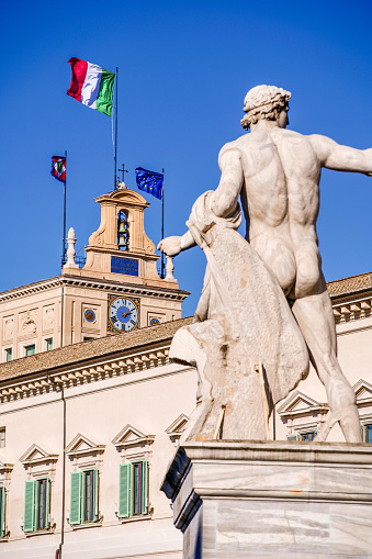 The flags of Italy, the European Union and the Italian Presidency fly on the bell tower of the Palazzo del Quirinale (Quirinal Palace), in the historic heart of Rome. The Quirinal Palace is currently the official seat of the President of the Italian Republic, elected every seven years by the Parliament. In the foreground, one of the monumental statues of the Fountain of the Dioscuri, Castor and Pollux, whose origins date back to Ancient Rome and come from the Baths of the Emperor Constantine. The fountain is located in the center of Piazza del Quirinale (Quirinal Square), in front of the Presidential Palace. Built in neoclassical style on the Quirinal hill between 1573 and 1583 as the summer residence of Pope Gregory XIII, this palace over the centuries has been the residence of the Popes (1605-1870), the residence of the King of Italy (1871-1946) and official seat of the Presidency of the Republic (from 1946 to today). Some of the most important Italian architects and artists participated in its construction and decoration, including Gian Lorenzo Bernini, Carlo Maderno, Guido Reni and Domenico Fontana. The Quirinal Palace, with an extension of 110,000 square meters, is the sixth largest building in the world. In 1980 the historic center of Rome was declared a World Heritage Site by Unesco. Image in High Definition format.