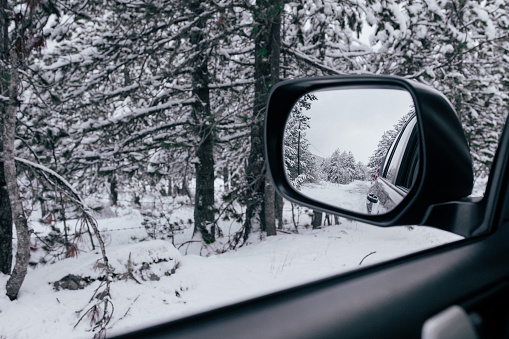 View in a outside mirror car on a mountain road with a snowy mountain landscape