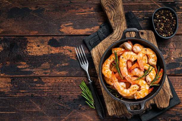Roast Prawns Shrimps in a pan with herbs and garlic. Dark wooden background. Top view. Copy space Roast Prawns Shrimps in a pan with herbs and garlic. Dark wooden background. Top view. Copy space. cajun food photos stock pictures, royalty-free photos & images