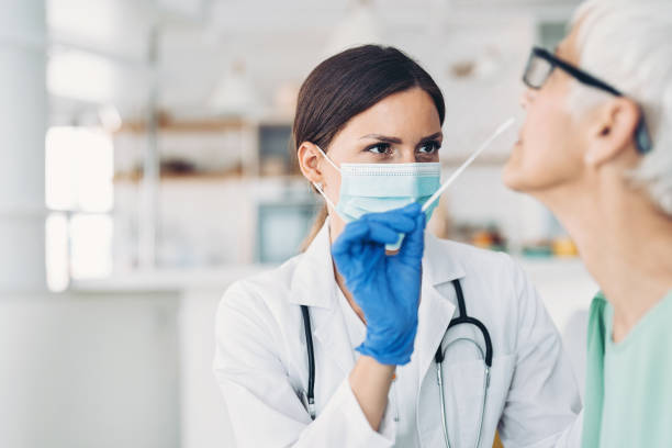 Female doctor taking a coronavirus sample from a senior patient stock photo