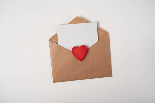 istock Craft envelope with a blank sheet inside and red wooden heart on the light (white) background. 1364930104
