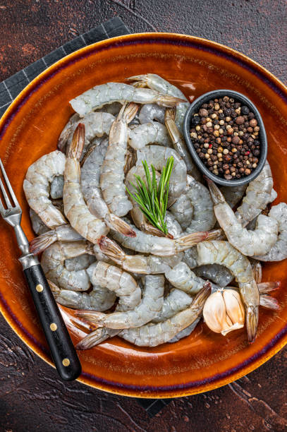 istock Black Raw uncooked Headless giant shrimps prawns in a rustic plate. Dark background. Top view 1364933506