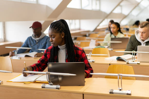 Young afro-American student is writing in the library stock photo