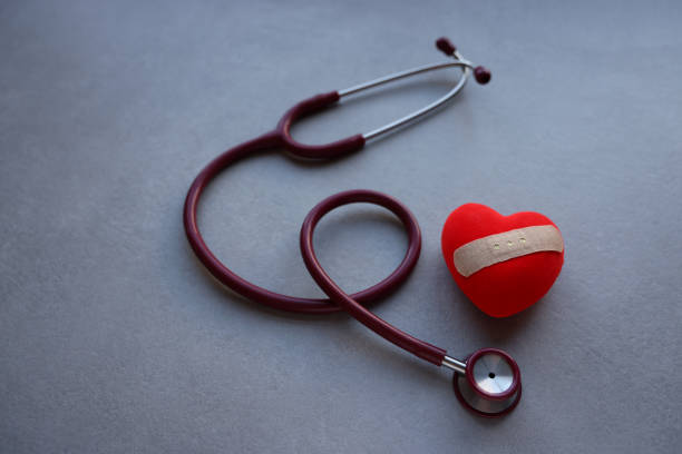 灰色の背景に赤い心臓と聴診器。 - 健康被害 ストックフォトと画像