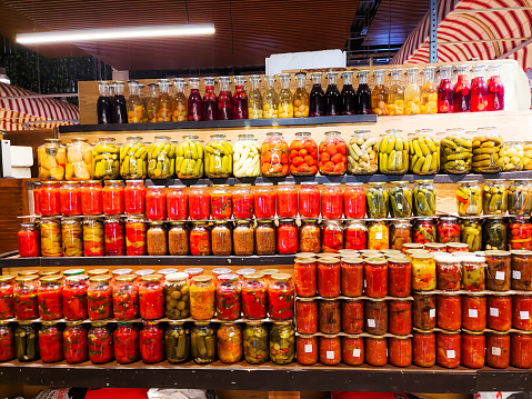 Glass jars with salted, pickled and canned vegetables and fruits are on the shelf.