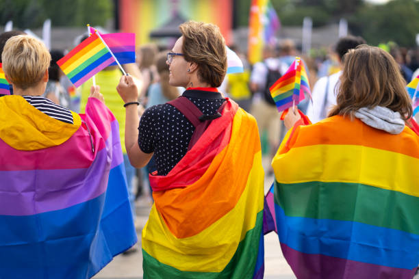 Group of people celebrating the pride month on a pride event Wrapped in bisexual flag and pride flags this trio are waving small pride flags and watching a gay pride event Attend LGBTQ  Events stock pictures, royalty-free photos & images