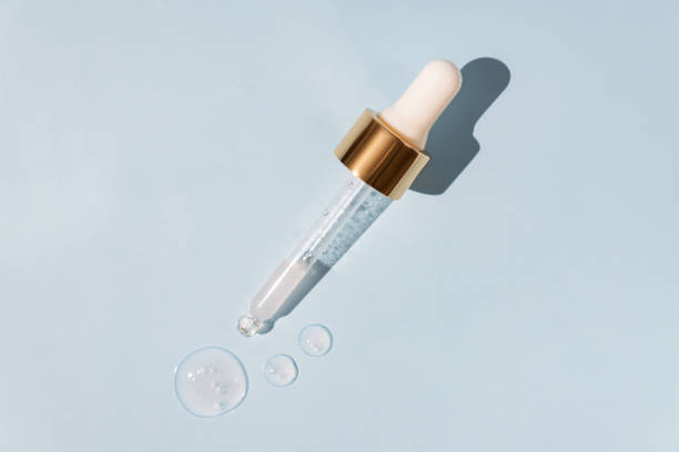Pink beauty face oil dripping from gold dropper on blue background. Skin care cosmetic advertisement with copy space Pink beauty face oil dripping from gold dropper on blue background. Skin care cosmetic advertisement with copy space. face serum dropper stock pictures, royalty-free photos & images