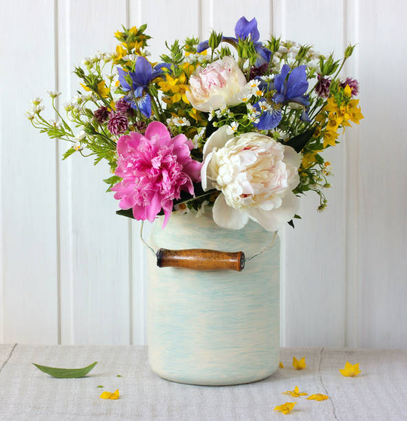 summer garden bouquet with peonies, daisies and irises in a can on a light background. floral arrangement in a rustic interior.