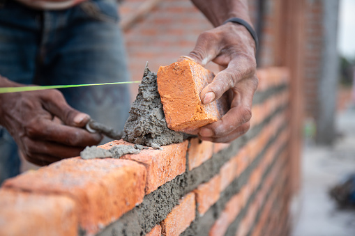 Bricklayer puts bricks to make a wall