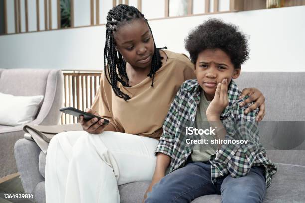 Little Miserable Boy Touching His Cheek While His Mom Comforting Him Stock Photo - Download Image Now