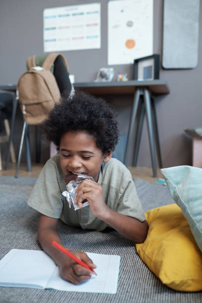 istock Cute African boy eating milk chocolate while drawing in copybook 1364939914