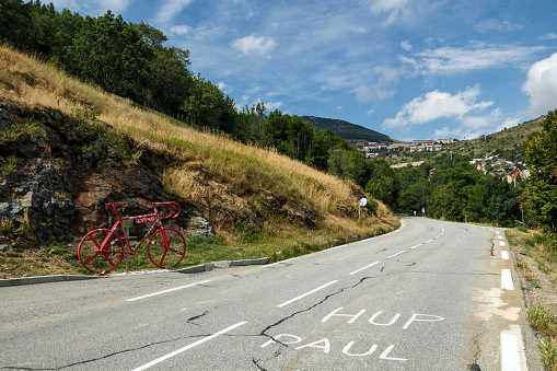 L'Alpe d'Huez, France - August 19, 2019: Ascent of the famous climb to L'Alpe d'Huez and itinerary of the Tour de France, pictured is the red bicycle close to the Eglise Saint-Ferréol church