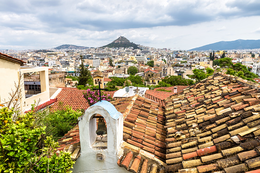 Athens view from Plaka district at Acropolis foot, Greece. This place is tourist attraction of city. Cityscape of Athens, Lycabettus mount in distance. Tile roof of Greek church in Athens city center