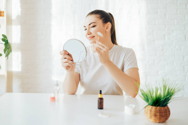 istock Girl with mirror rolls her face with stone roller 1364943993