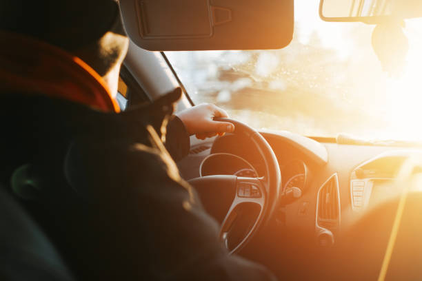 istock Back view of male driver in jacket and hat driving car, inside. Selective focus on hand holding steering wheel 1364946217