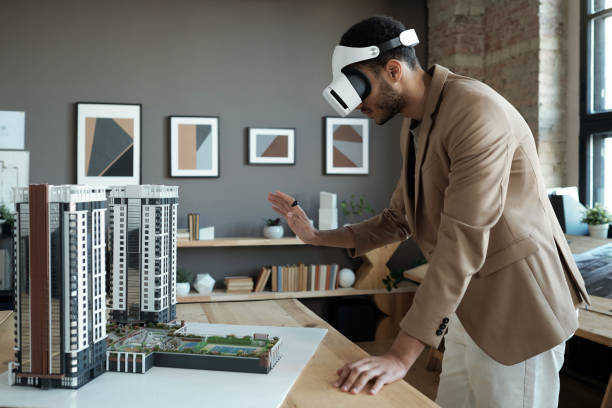 istock Young elegant architect standing by table with house layout during presentation 1364947226