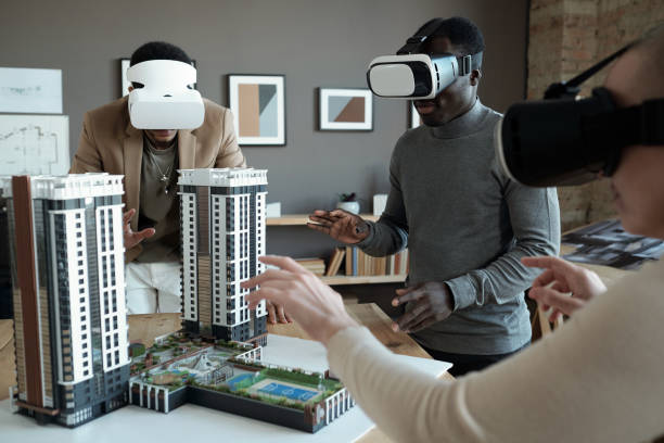istock Group of architects in vr headsets standing around table with house layout 1364947236