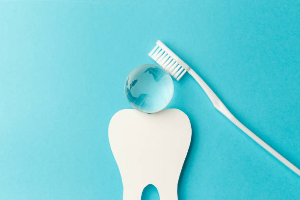 치과 의사의 국제 날의 개념. 흰색 칫솔, 종이 치아 및 유리 글로브는 파란색 배경에 있습니다. 맨 위 보기입니다. 플랫 레이. 클로즈업. 복사 공간 - toothbrush dental hygiene glass dental equipment 뉴스 사진 이미지